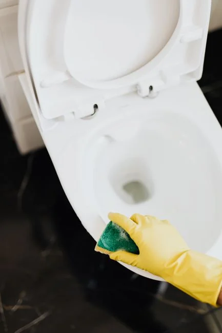 Close-up of hand cleaning window with squeegee outdoors using yellow gloves.